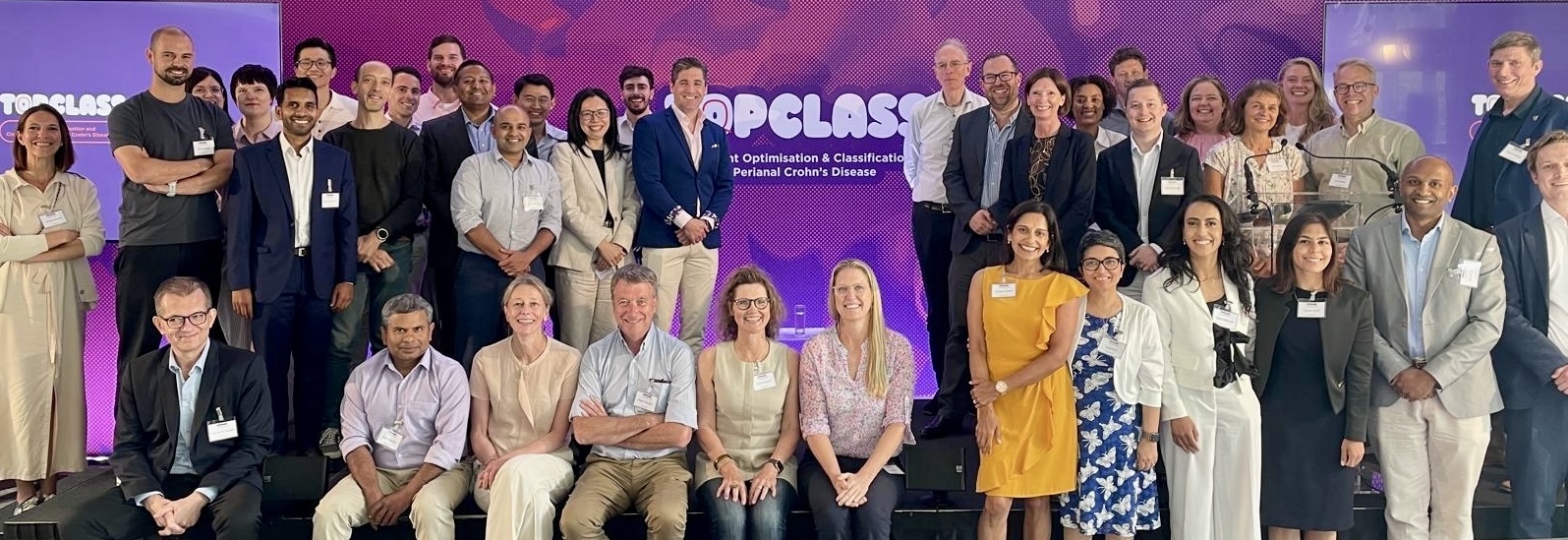 Group photograph of the TOpClass Consortium members at a meeting, standing and seated in front of a TOpClass banner reading Treatment Optimisation and Classification of Perianal Crohn's Disease.